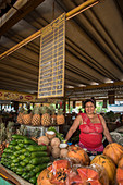 A smiling woman produce vendor stands over her fruits and vegetables at the Agropecuario 19 y B food market in the Vedado section of Havana Cuba.