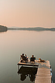 Man And Woman Enjoying Coffee With Their Dog On The Edge Of A Dock On Caspian Lake