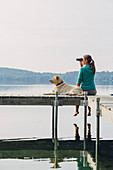 Woman With Her Dog Sitting On Dock Using Binoculars In Caspian Lake