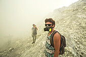 Two Men With Gas Mask Hiking In Volcano Kawah Ijen, Java, Indonesia