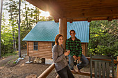 A Young Couple Enjoy An Evening On The Porch Of A Cabin At The Lodge Near Greenville, Maine