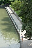 Young woman runs at edge of river, urban setting