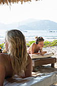 Young woman relaxes on beach, woman looks out in foreground