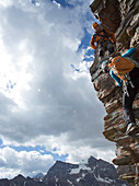 Mountain guide assists woman climber up rock face above mountains