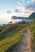 Die Mitternachtssonne leuchtet die grünen Wiesen und den Weg zum blauen Meer Uttakleiv Lofoten Inseln Norwegen Europa