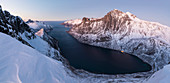 Draufsicht auf die schneebedeckten Gipfel um Fjordgard umrahmt von der gefrorenen See bei Sonnenuntergang Ornfjorden Senja Tromsø Norwegen Europa