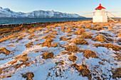 Die Sonne beleuchtet die Küste in der Nähe eines traditionellen Leuchtturms, Spaknesora naturreservat, Djupvik, Lyngenfjord, Lyngen Alpen, Troms, Norwegen, Lappland, Europa
