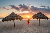 Bavaro Beach, Bavaro, Higuey, Punta Cana, Dominican Republic, Woman by thatch umbrellas on the beach at sunrise , MR