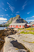 Typische Häuser der Fischer genannt Rorbu umrahmt von felsigen Gipfeln und blauen Meer Reine Moskenes Lofoten Inseln Norwegen Europa