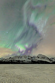 Der eisige See von Jaegervatnet umrahmt von den Nordlichtern (Aurora Borealis) und Sternenhimmel in der Polnacht, Lyngen Alpen, Troms, Norwegen, Skandinavien, Europa