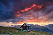 Hölzerne Hütte umrahmt von feurigen Himmel und Wolken bei Sonnenuntergang, Muottas Muragl, St. Moritz, Kanton Graubünden, Engadin, Schweiz, Europa
