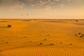 Heißluftballons über Sanddünen bei Sonnenaufgang in der Dubai Wüste, Dubai, Vereinigte Arabische Emirate, Mittlerer Osten
