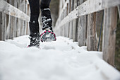 Person snowshoeing on footbridge in winter