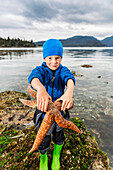 Junge zeigt einen großen Seestern, Hesketh Island, South Central Alaska, USA