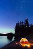 'Ein glühendes Zelt am Strand mit Blick auf die grüne Aurora Borealis spiegelt sich in der ruhigen Ozean Wasser, Hesketh Island; Homer, Alaska, Vereinigte Staaten von Amerika'