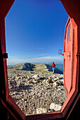 Woman hiking towards red bivouac, Monte Amaro, Majella, Abruzzi, Italy