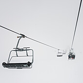 'Skiiers on a chair lift against a white cloud filled sky at a ski resort; Whistler, British Columbia, Canada'