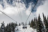 'Downhill skiers riding a chairlift at a ski resort; Whistler, British Columbia, Canada'
