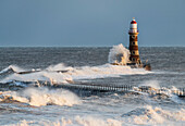 Wellen, die gegen Roker Leuchtturm am Ende eines Piers spritzen, Sunderland, Tyne und Wear, England