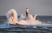 Wellen, die gegen Roker Leuchtturm am Ende eines Piers spritzen, Sunderland, Tyne und Wear, England