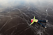 A young woman lays on her back on a frozen surface looking up while ice skating, Alaska, United States of America