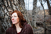 Portrait of a woman with red hair against a tree and looking contemplative, Homer, Alaska, United States of America