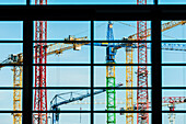 Coloured construction cranes on a building site seen through a window, Hamburg, Germany