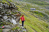 Woman hiking looking at hut Naturfreundehaus Neubau, Tauern ridgeway, High Tauern range, Salzburg, Austria