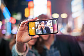 Junges Paar, das selfie in beleuchteter Stadtstraße nimmt