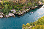 das türkisfarbene Wasser des Flusses Neretva und ein kleines Boot für Touristen, Mostar, Federation of Bosnia and Herzegovina
