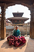 Bhaktapur, Kathmandu, Bagmati area, Nepal Old lady sitting in prayer under a temple in Bhaktapur