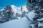 Die Kirche Saint Gaudenzio, umgeben von schneebedeckten Kiefern in der blauen Stunde, Engadin, Schweiz