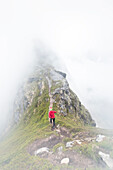 Hiker runs on a steep path to reach the peak of the Reinebringen mountain under the mist Moskenes Lofoten Islands Norway Europe