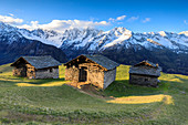 Meadows and alpine huts framed by snowy peaks at dawn Tombal Soglio Bregaglia Valley canton of Graubünden Switzerland Europe