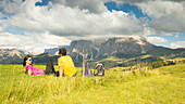 ein Paar sitzt und entspannt auf einer Wiese auf der Seiser Alm, (Seiser Alm), Bozen, Südtirol, Trentino-Südtirol, Italien
