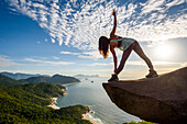 Frau in Yoga-Haltung am Rande des Berges in Pedra do Telégrafo, Barra de Guaratiba, Westseite von Rio de Janeiro, Brasilien