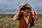 A 6 year old Japanese American boy dressed as an explorer with a hat and vest surveys the land (grasslands and prairies) with his binoculars in Badlands National Park, South Dakota.