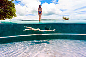 Young woman swimming in outdoor swimming pool beside woman standing outside