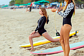 Junge Frauen dehnen am Strand neben Surfbrettern