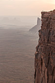A small hiker stands at a sharp cliff edge at Green River Overlook in Canyonlands National Park, Utah.