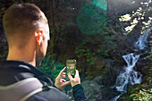 Over the shoulder view of man photographing waterfall with smartphone while hiking, Cataract Falls Trail, Mount Tamalpais Watershed, Marin County, California, USA