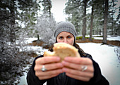Photograph with young female hiker holding sandwich towards camera in natural scenery in winter, Bryce Canyon National Park, Utah, USA