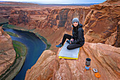 Female hiker sitting on cliff at Horseshoe Bend of Colorado River, Arizona, USA