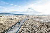 Clouds over boy walking alone on boardwalk across grass in front of Mono Lake, California, USA