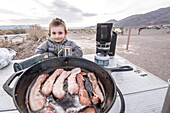 Junge lächelt beim Speck Frühstück beim Campen im Death Valley National Park, Kalifornien, USA