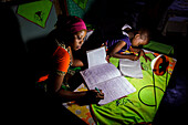 'Mforo, Tansania ein Dorf in der Nähe von Moshi, Tansania. Mit einer Solar-Schwester-Solar-Laterne studieren mehrere Kinder der Solar-Schwester Unternehmerin Fatma Mziray in der Nacht. Ihre ältere Tochter Zainabu Ramadhani Alter19 ist auf der linken und m