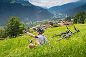 Mountain Biker Sitting At An Alpine Meadow Pointing Towards A Summit He Wants To Reach