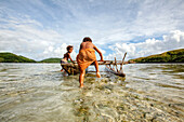 Kinder spielen mit einem Auslegerkanu im Dorf Hessessai Bay auf der Insel PanaTinai (Panatinane) im Louisiade-Archipel in der Provinz Milne Bay, Papua-Neuguinea. Die Insel hat eine Fläche von 78 km2. Der Louisiade-Archipel besteht aus zehn größeren Vulkan