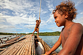 Kinder spielen mit einem Auslegerkanu im Dorf Hessessai Bay auf der Insel PanaTinai (Panatinane) im Louisiade-Archipel in der Provinz Milne Bay, Papua-Neuguinea. Die Insel hat eine Fläche von 78 km2. Der Louisiade-Archipel besteht aus zehn größeren Vulkan