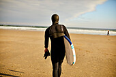 Ein Surfer, der mit seinem Surfbrett am Strand geht